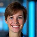 A smiling female blockchain developer, mid-thirties, with a contemporary office background, representing technical expertise.