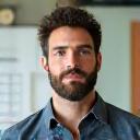 A confident male UX designer, early forties, with a creative workspace and a whiteboard in the background, signaling design and product focus.